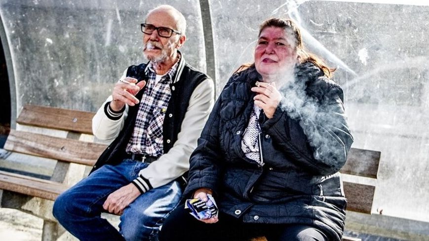 Twee rokende personen zitten buiten op een bankje